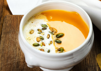 Pumpkin soup in white plate on wooden table with  seeds