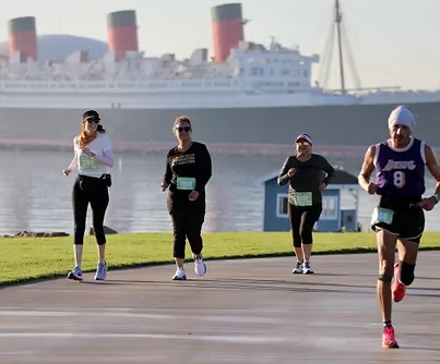 Four runners jog along a waterfront path with a large cruise ship in the background.